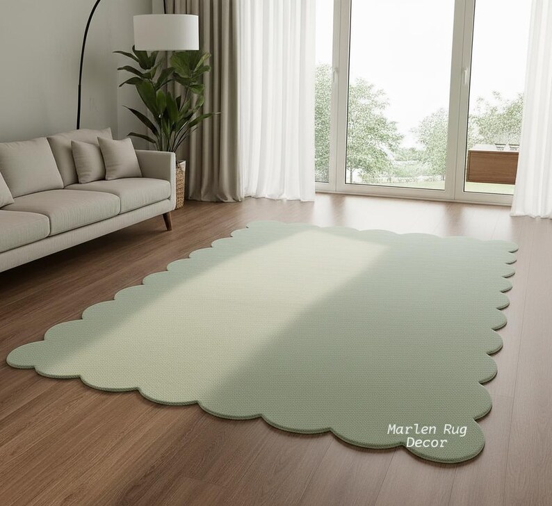 Puede incluir: Una alfombra grande, verde salvia, con un borde festoneado sobre un suelo de madera. La alfombra rectangular tiene esquinas redondeadas y una superficie texturizada. Las palabras "Marlen Rug Decor" est&aacute;n impresas en la alfombra.
