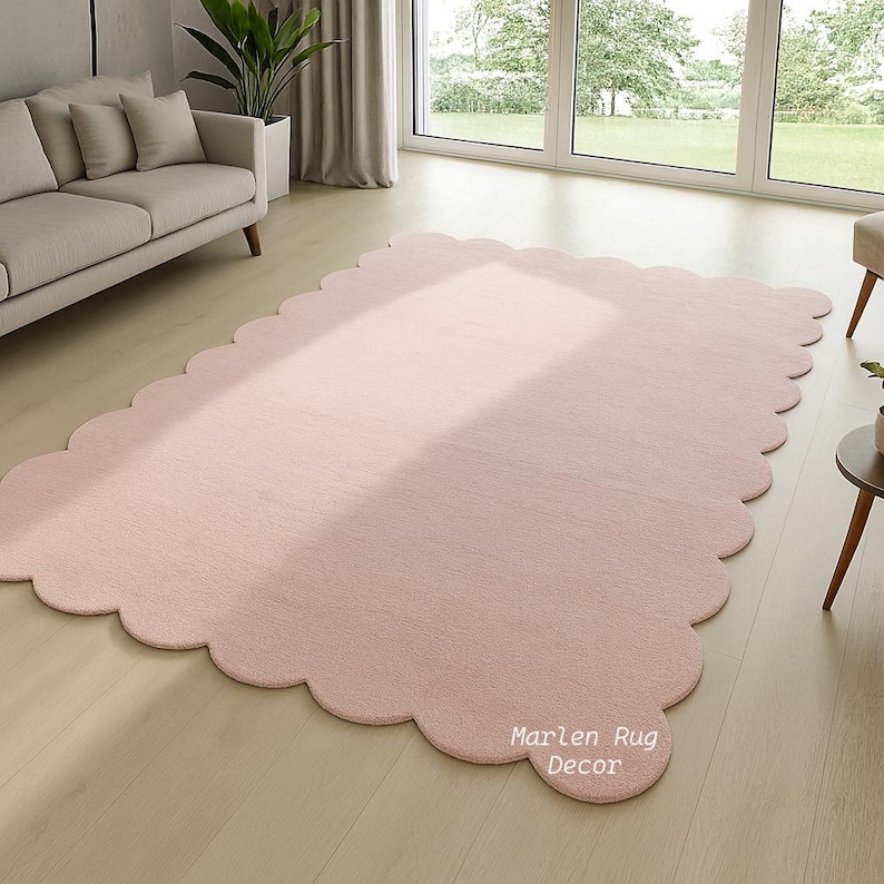 Puede incluir: Una alfombra grande de color rosa claro con un borde festoneado. La alfombra tiene forma rectangular con esquinas redondeadas y una textura suave y afelpada. El texto "Marlen Rug Decor" est&aacute; impreso en el borde de la alfombra. La alfombra est&aacute; colocada sobre un suelo de madera clara.