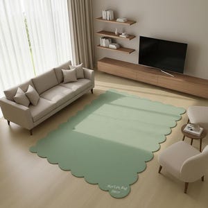 Puede incluir: Una alfombra verde salvia con bordes festoneados en un sal&oacute;n. La alfombra est&aacute; colocada sobre un suelo de madera clara, con un sof&aacute; beige, dos sillones y un mueble de TV de madera. La alfombra tiene el texto "MarLen, Rug Decor".