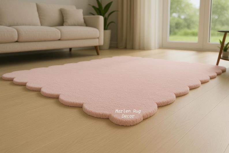 Puede incluir: Una alfombra rosa claro con bordes festoneados sobre un suelo de madera. La alfombra tiene una textura suave y afelpada y est&aacute; en un sal&oacute;n con un sof&aacute; beige y luz natural.