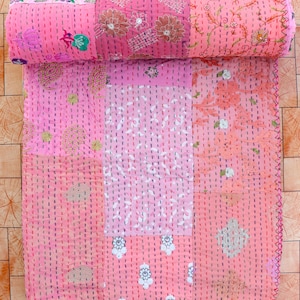 Può includere: Una trapunta patchwork rosa con motivi floreali e geometrici. La trapunta è cucita a mano con filo visibile e arrotolata nella parte superiore. La trapunta è composta da più quadrati di tessuto.