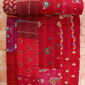 Peut inclure: Une courtepointe patchwork roulée, dans les tons de rouge, bordeaux et rose. La courtepointe présente des motifs floraux et cachemire brodés complexes de différentes couleurs. Les coutures sont visibles partout, ajoutant de la texture et des détails au textile artisanal.