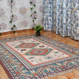 May include: A rectangular area rug with a geometric pattern in shades of cream, teal, orange, and brown. The rug features a central diamond design and a fringed edge. The rug is placed on a tiled floor.