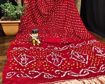 May include: A vibrant red textile with a repeating pattern of white and yellow dots. The fabric features a decorative border with a gold-colored trim. A small figurine is placed on the fabric, and a potted plant is visible in the background.