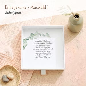 Pu&ograve; includere: Una scatola regalo quadrata bianca contenente un biglietto con un'illustrazione ad acquerello di un ramo di eucalipto e il testo in tedesco: Herzlichen Gl&uuml;ckwunsch zu eurem besonderen Jubil&auml;um! Es ist inspirierend zu sehen, dass ihr nach all der Zeit noch immer so ein starkes Team seid. Wir w&uuml;nschen euch f&uuml;r den weiteren gemeinsamen Weg nur das Beste und viel Freude. Im Herzen alles Liebe.