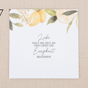 May include: A square white card featuring a watercolor illustration of yellow lemons and green leaves along the top edge. The text reads: Liebe H&Auml;LT DIE ZEIT AN UND L&Auml;SST DIE Ewigkeit BEGINNEN. The design is centered on a clean, plain white background.