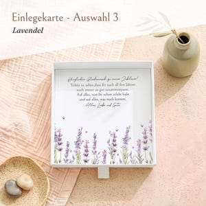 Pu&ograve; includere: Una scatola regalo quadrata bianca con un coperchio che presenta un'illustrazione floreale di lavanda sul fondo e il testo in tedesco: Herzlichen Gl&uuml;ckwunsch zu eurem Jubil&auml;um! Sch&ouml;n zu sehen, dass ihr nach all den Jahren noch immer so gut zusammenpasst.