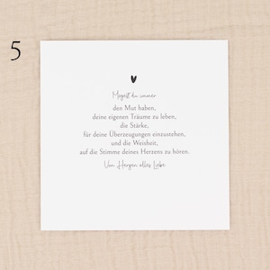 May include: A white card with black text and a small heart illustration. The text is in German and includes phrases about courage, dreams, and listening to one's heart. The number "5" is in the upper left corner. The card is on a beige fabric background.