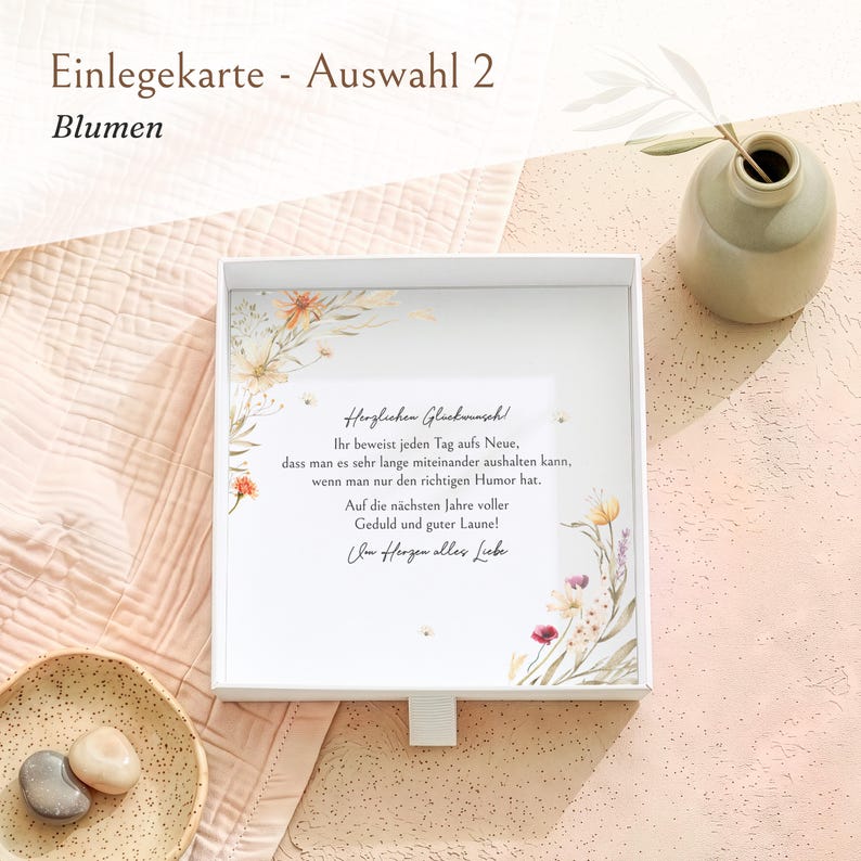 Pu&ograve; includere: Una scatola regalo quadrata bianca con un inserto stampato decorato da illustrazioni floreali ad acquerello negli angoli e il testo in tedesco: Herzlichen Gl&uuml;ckwunsch! Ihr beweist jeden Tag aufs Neue, dass man es sehr lange miteinander aushalten kann, wenn man nur den richtigen Humor hat. Auf die n&auml;chsten Jahre voller Geduld und guter Laune! Von Herzen alles Liebe.