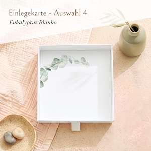 Pu&ograve; includere: Una scatola quadrata bianca con un cassetto estraibile caratterizzato da un disegno di ramo di eucalipto stampato nell'angolo in alto a sinistra. Il testo "Einlegekarte - Auswahl 4" e "Eukalyptus Blanko" &egrave; visibile in alto.