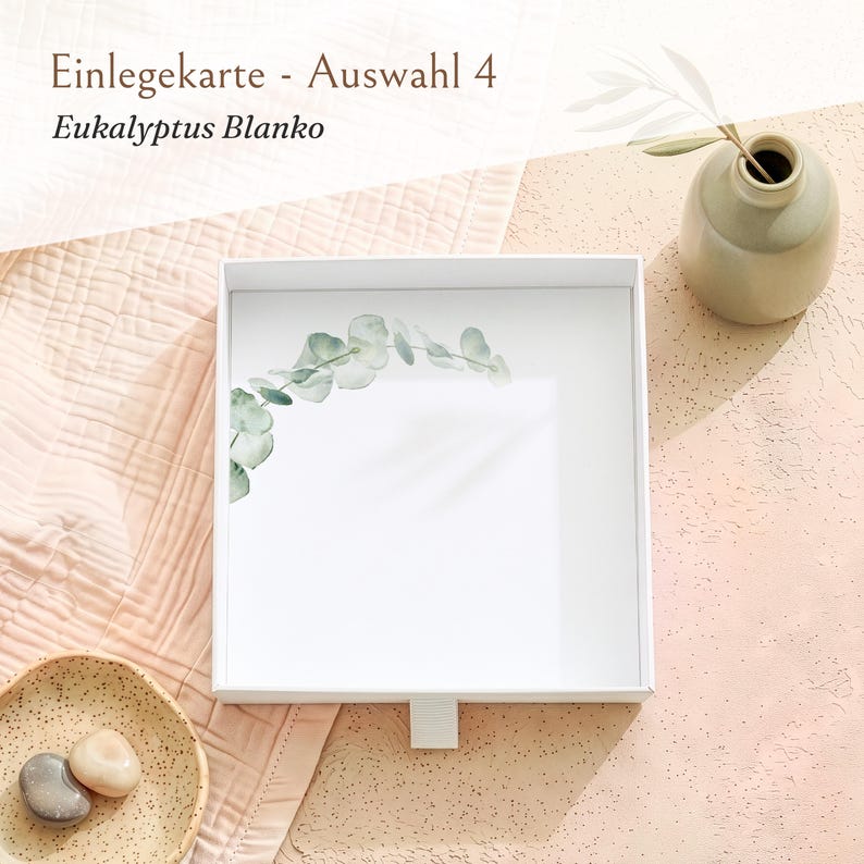 Pu&ograve; includere: Una scatola quadrata bianca con un cassetto estraibile caratterizzato da un disegno di ramo di eucalipto stampato nell'angolo in alto a sinistra. Il testo "Einlegekarte - Auswahl 4" e "Eukalyptus Blanko" &egrave; visibile in alto.