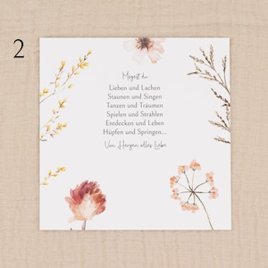 May include: A square card with watercolor floral illustrations and text in German. The card features a white background with delicate flowers in shades of peach, yellow, and brown. The text is centered and reads "Mogest du..." followed by a poem.