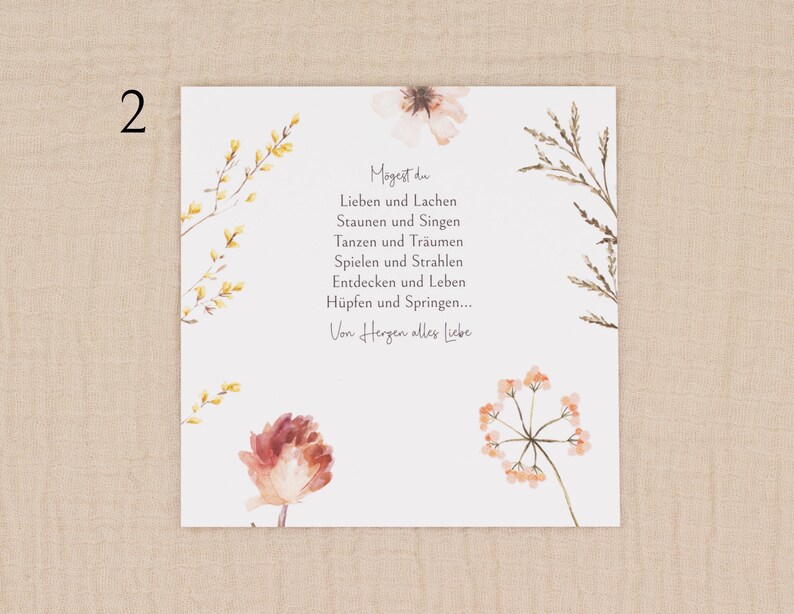 May include: A square card with watercolour floral illustrations and German text. The card has a white background with delicate flowers in peach, yellow, and brown. The text is centred and reads "Mogest du..." followed by a poem.