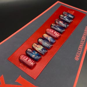 Puede incluir: Juego de uñas postizas con acabado brillante, con imágenes de personajes y el texto "TRUE BLOOD" en rojo. Las uñas están dispuestas sobre una tarjeta rectangular roja, sobre un fondo oscuro.