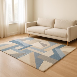 May include: A rectangular rug with a geometric pattern in blue, beige, and grey. The rug is on a wooden floor in front of a beige sofa. The design features various shapes and angles. The rug is a stylish addition to any living space.