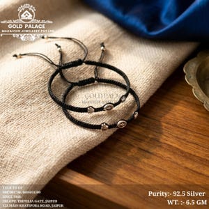 Op de afbeelding: Twee zwarte koordarmbanden met kleine zilverkleurige metalen accenten met gegraveerde ster- en schelpachtige patronen. De armbanden hebben verstelbare schuifknopen en kleine zilveren kralen. Tekst op afbeelding: Purity:- 92.5 Silver WT. :- 6.5 GM.