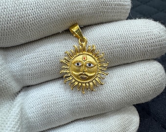 May include: A gold-colored sun pendant with a detailed face and radiating rays. The pendant features a mustache, eyes, and a red dot. The pendant is approximately 1 inch in diameter.