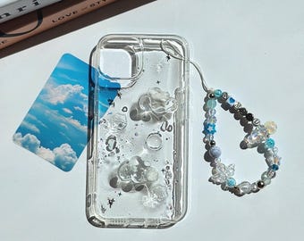 May include: A clear phone case featuring raised cloud-shaped accents, silver star-shaped glitter, and a detachable beaded phone charm. The charm consists of blue, white, and clear beads, including letter beads spelling AMU, star shapes, and a butterfly.