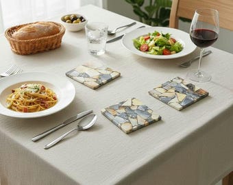 May include: A dining table set for a meal, featuring a white tablecloth, plates of food, a glass of red wine, and decorative coasters. The table setting includes a basket of bread, salad, pasta, and olives.