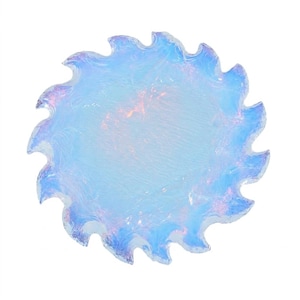 Puede incluir: Un objeto decorativo redondo y translúcido con un borde festoneado. El objeto tiene un tono azul claro con toques de rosa y morado, y parece estar hecho de vidrio. El diseño recuerda a una flor o sol estilizado.