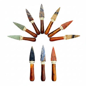 May include: A collection of handcrafted arrowheads with wooden handles and various stone tips. The tips display a range of colors and patterns, including green, brown, red, and blue. Each arrowhead is approximately 5 inches long.