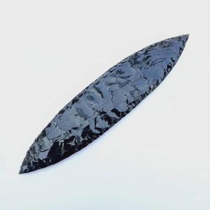 May include: A black obsidian arrowhead, long and slender with a sharp point. The surface has a textured appearance, reflecting light. This object is likely a historical artifact or a decorative item, possibly from an archaeological find.