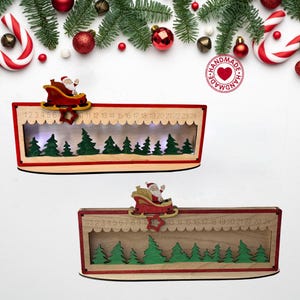 May include: Two rectangular wooden Christmas advent calendars featuring a sliding red star marker to track days one through twenty-four. Each calendar displays a cutout scene of green pine trees and a wooden Santa Claus in a red sleigh on top.