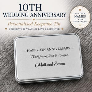 May include: A rectangular silver-colored metal keepsake tin featuring black engraved text that reads HAPPY TIN ANNIVERSARY, Ten Years of Love & Laughter, and the names Matt and Emma. The lid is smooth and metallic with rounded corners.