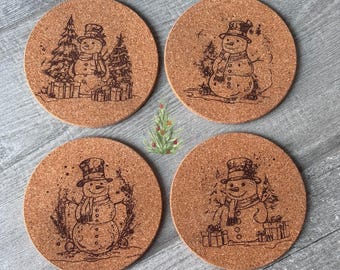 May include: Four round cork coasters with etched snowman designs. Each coaster features a snowman wearing a top hat and scarf, with gifts and trees. The coasters are a natural brown color, perfect for holiday decor.