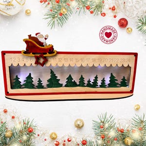 May include: A wooden Christmas advent calendar featuring a red frame and a cutout of Santa Claus in a sleigh. The calendar displays numbers 1 through 24 along the top edge, with a row of green painted pine trees inside and integrated LED lights.