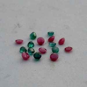 May include: A collection of round, faceted gemstones in shades of green and pink. The gemstones are scattered on a white surface.