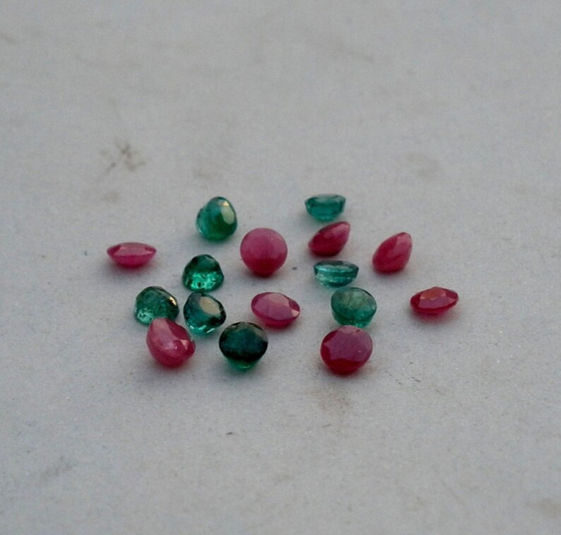 May include: A collection of round, faceted gemstones in shades of green and pink. The gemstones are scattered on a white surface.