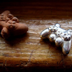 May include: Two small figurines, one brown and one silver, are on a wooden surface. The silver figurine is shaped like a video game controller.