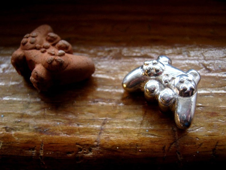 May include: Two small figurines, one brown and one silver, are on a wooden surface. The silver figurine is shaped like a video game controller.