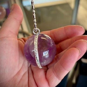 May include: A silver chain with a large, round, purple amethyst pendant. The pendant is cut in half and the two halves are joined together with a silver band.