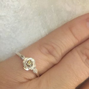 May include: A silver ring with a delicate rose design and a small, round, brown gemstone in the center.