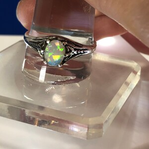 Puede incluir: Un anillo de plata con una piedra de &oacute;palo ovalada. El &oacute;palo tiene una base blanca con destellos de color verde, azul y amarillo.
