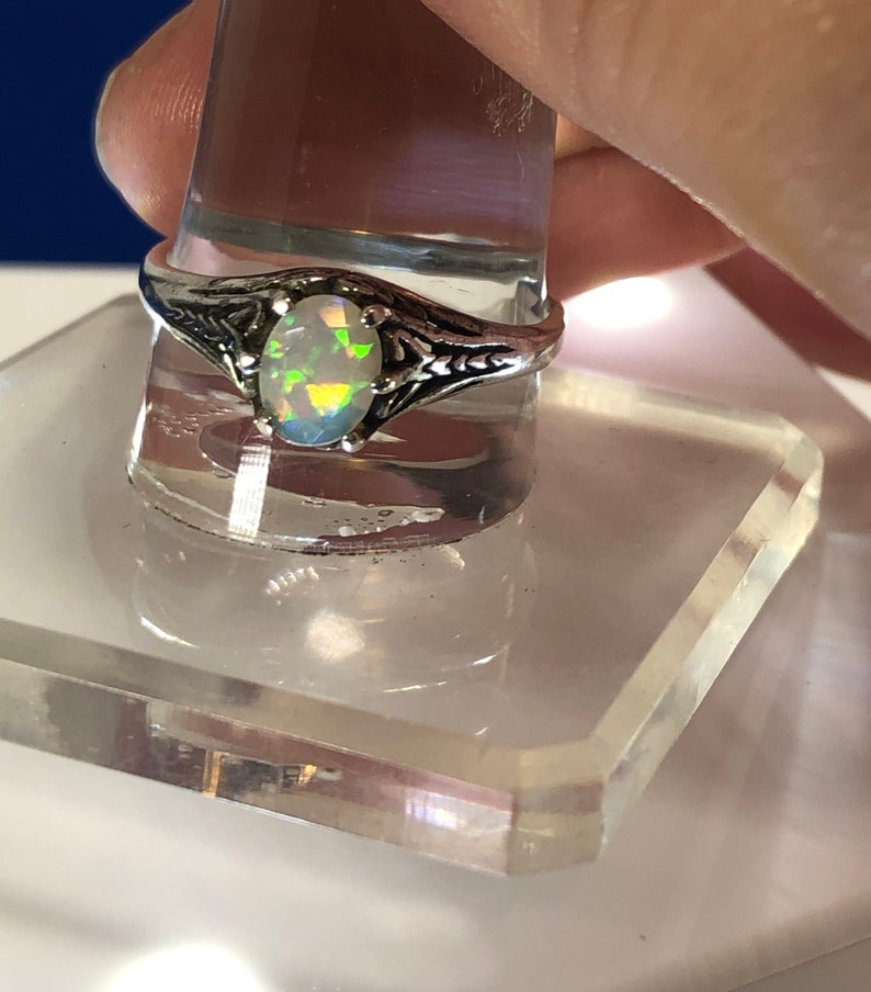 Puede incluir: Un anillo de plata con una piedra de &oacute;palo ovalada. El &oacute;palo tiene una base blanca con destellos de color verde, azul y amarillo.