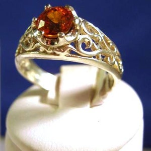 Op de afbeelding: Een zilveren ring met een oranje edelsteen gezet in een filigraan ontwerp.