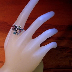 Puede incluir: Un anillo de plata con un diseño de espiral y piedras preciosas de colores. El anillo está en una mano de maniquí blanca.