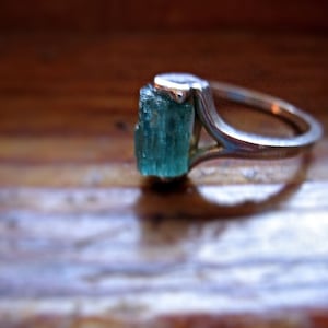 May include: A silver ring with a light blue gemstone set in the center. The gemstone is a long, rectangular shape.