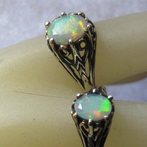 Puede incluir: Un anillo de plata con dos piedras de &oacute;palo engastadas en intrincados dise&ntilde;os de filigrana. Los &oacute;palos son de color verde p&aacute;lido y blanco con destellos de color.