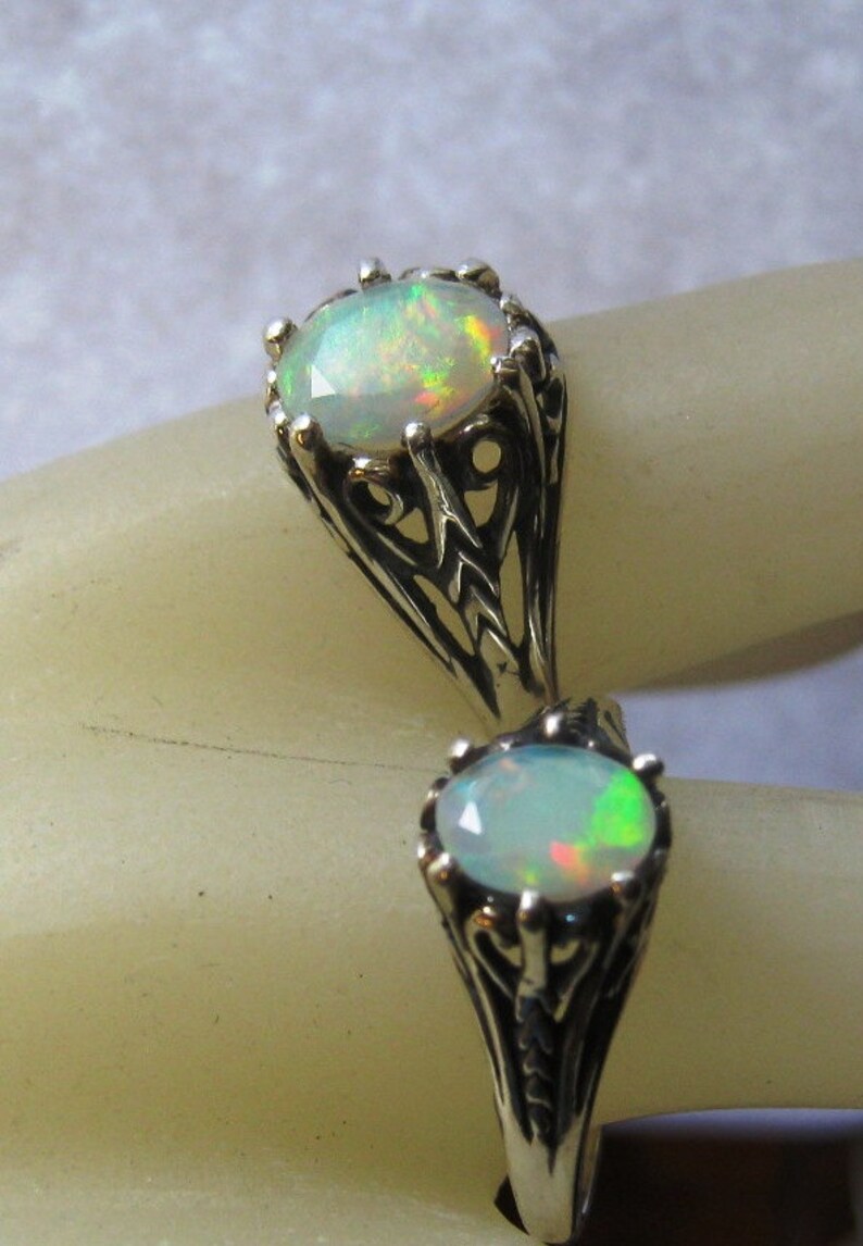 Puede incluir: Un anillo de plata con dos piedras de &oacute;palo engastadas en intrincados dise&ntilde;os de filigrana. Los &oacute;palos son de color verde p&aacute;lido y blanco con destellos de color.