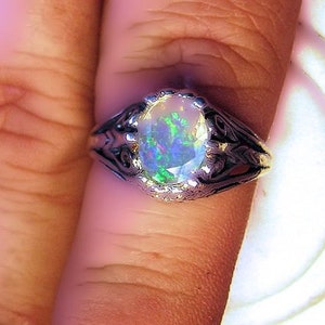 Puede incluir: Un anillo de plata con una piedra preciosa de &oacute;palo de forma ovalada. El &oacute;palo presenta un arco&iacute;ris de colores, incluyendo verde, azul y morado.