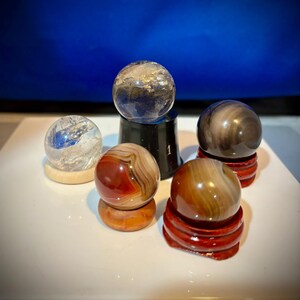 May include: Five small, polished spheres of various colors and patterns, displayed on individual stands. The spheres are made of agate, quartz, and other natural materials.