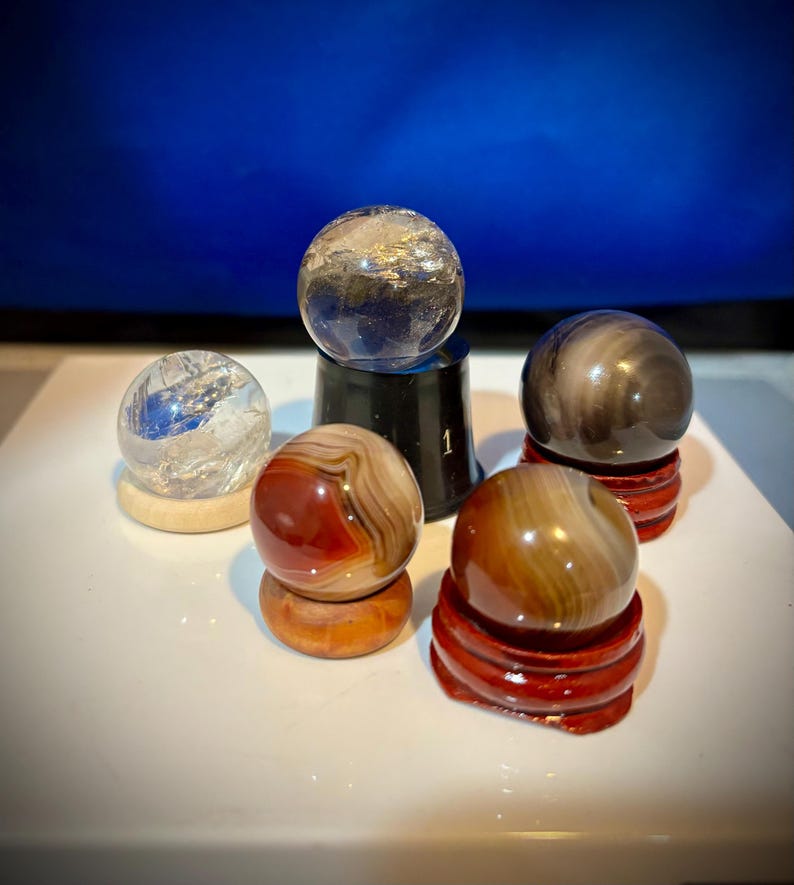 May include: Five small, polished spheres of various colors and patterns, displayed on individual stands. The spheres are made of agate, quartz, and other natural materials.