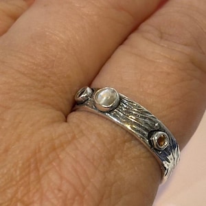 May include: A silver ring with a textured band and three stones. The center stone is a white opal, and the two smaller stones are brown.