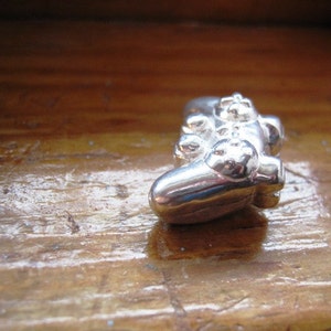 May include: A silver-colored, miniature replica of a video game controller. The controller is lying on a wooden surface.
