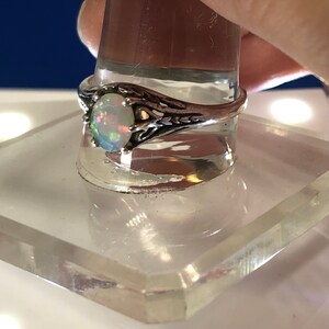 Puede incluir: Un anillo de plata con una piedra de &oacute;palo ovalada. El anillo tiene un dise&ntilde;o delicado e intrincado con un patr&oacute;n de filigrana.