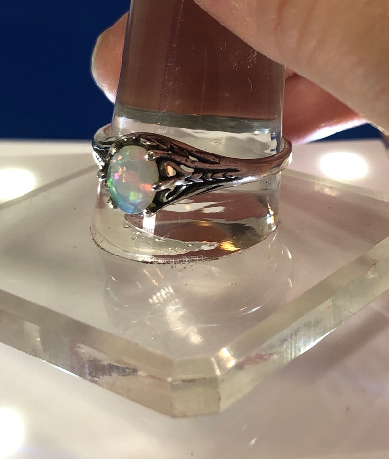 Puede incluir: Un anillo de plata con una piedra de &oacute;palo ovalada. El anillo tiene un dise&ntilde;o delicado e intrincado con un patr&oacute;n de filigrana.